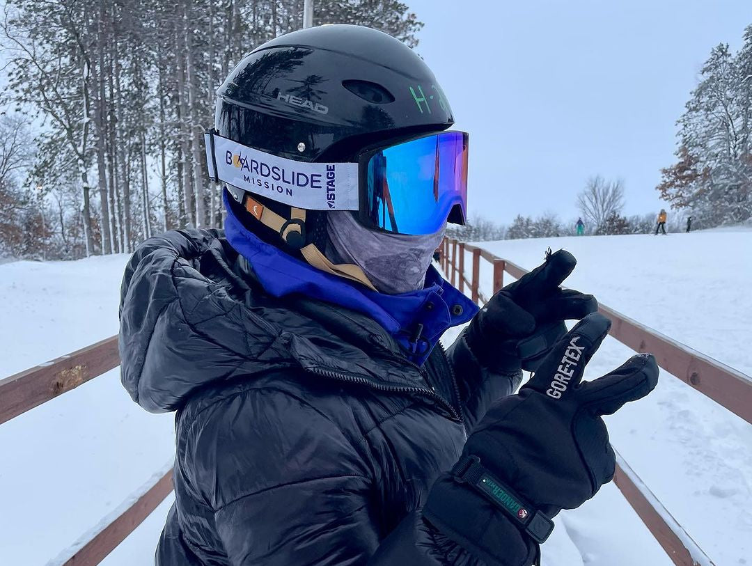 A man on the ski slopes wearing STAGE Custom Ski Goggles showcasing the Boardslide Mission logo.