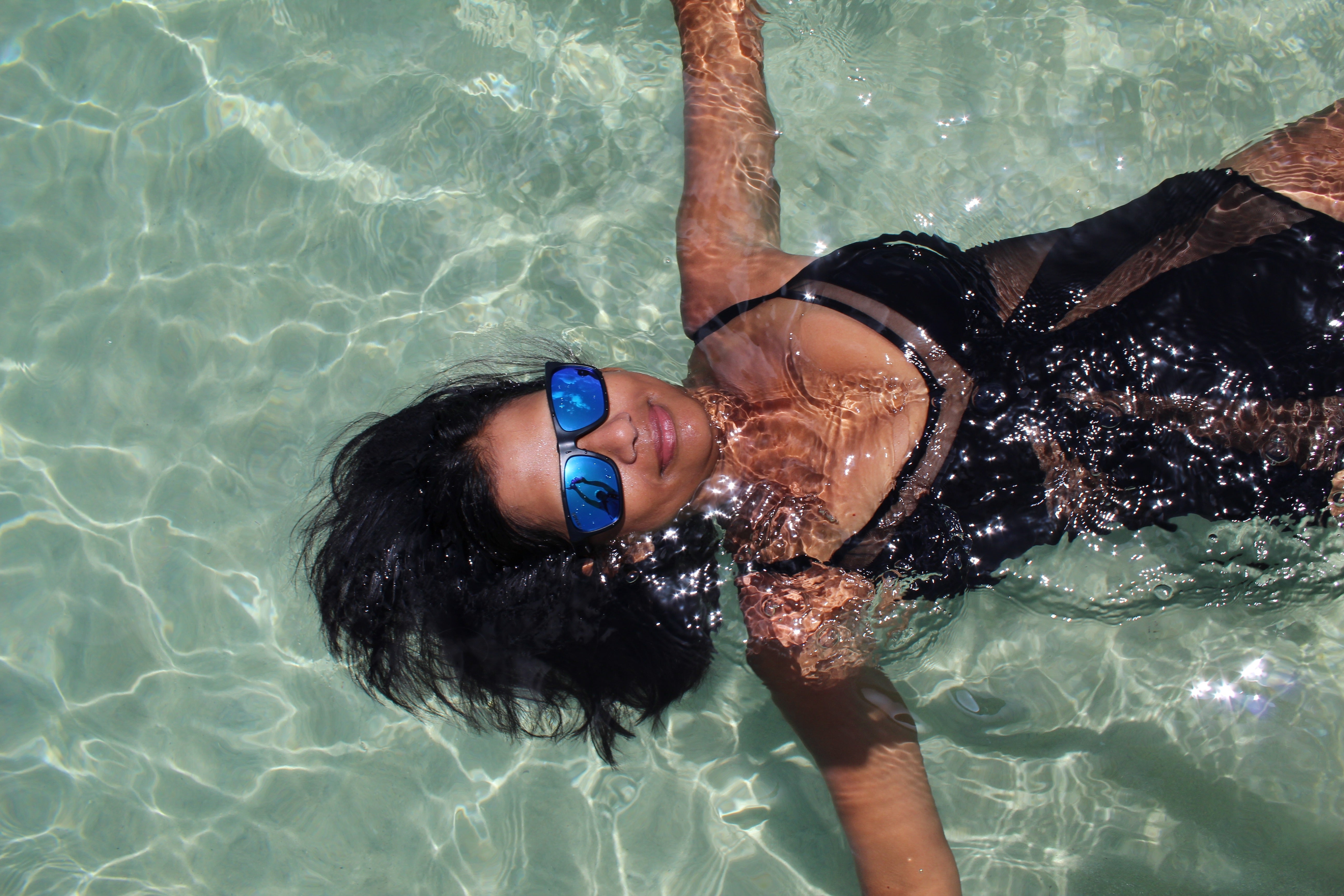 Girl floating in swimming pool while wearing STAGE Floating Sunglasses with Blue Revo lenses