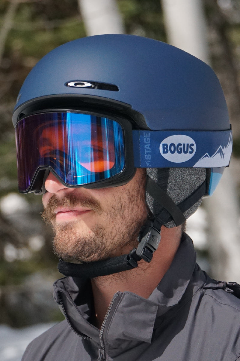 A man wearing STAGE custom ski goggles featuring Bogus Basin resort's logo. The man is also wearing a blue ski and snowboard helmet. 