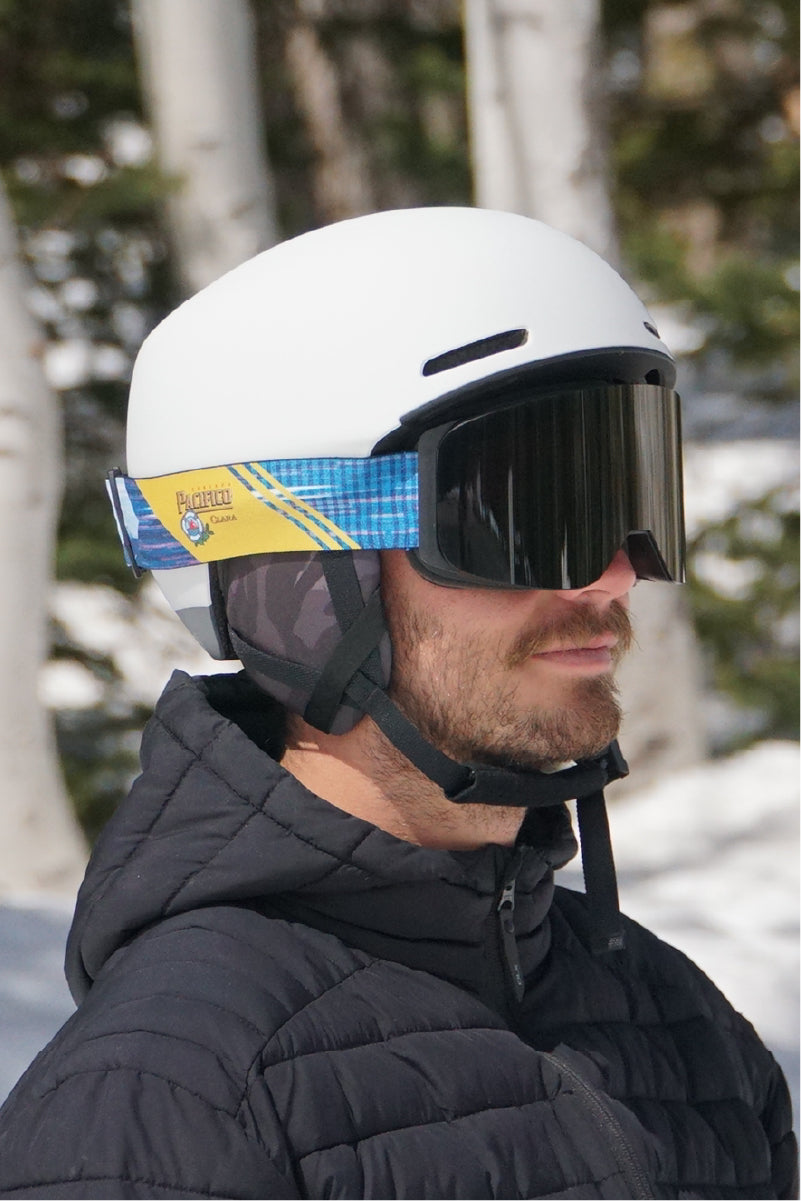 A man wearing STAGE custom snow goggles featuring Pacifico's logo. The man is also wearing a white ski helmet.