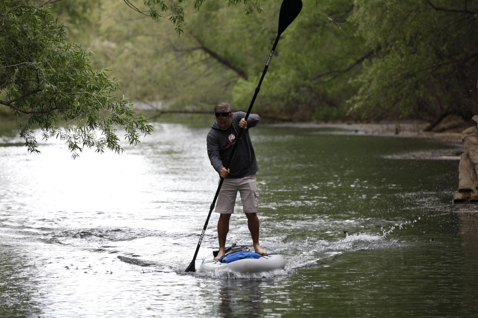 A man using the STAGE 2SIDE Double-Sided Paddleboard Paddle while standing on a STAGE Inflatable Stand-Up Paddleboard. The man is going fast through the waters of Southern Utah.