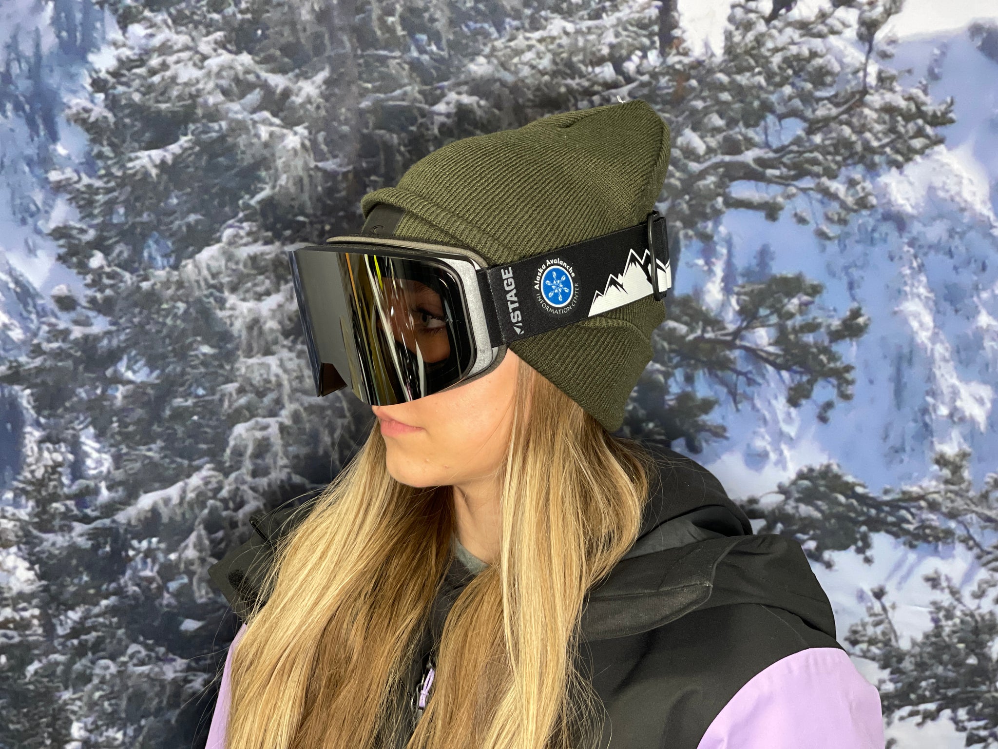Woman wearing a pair of STAGE Cusotm Ski Goggles featuring the Alaska Avalanche Information Center logo on the STAGE Propnetic Magnetic Ski goggles