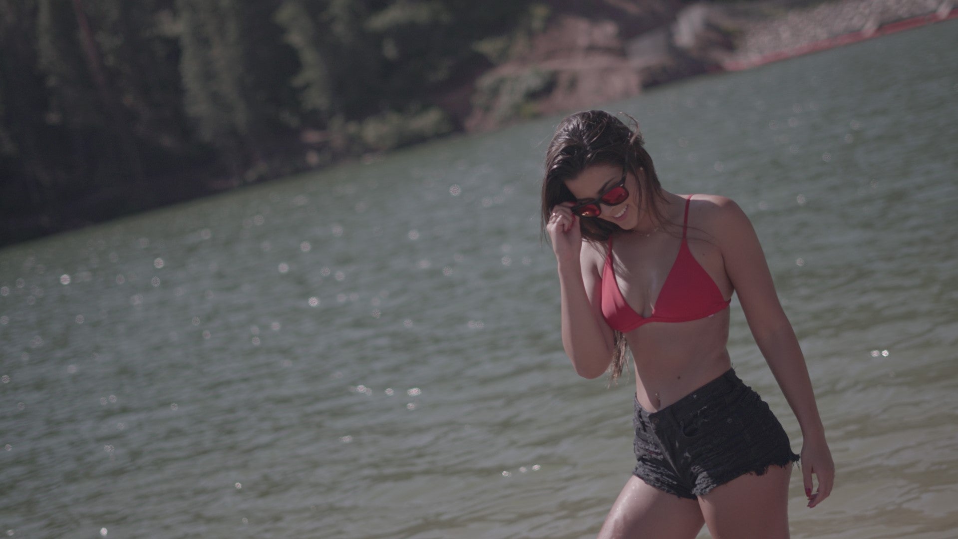 Girl in red bikini and black shorts wears STAGE Floating Sunglasses with Red Revo Lens at Tibble Fork Reservoir in American Fork Canyon, Utah