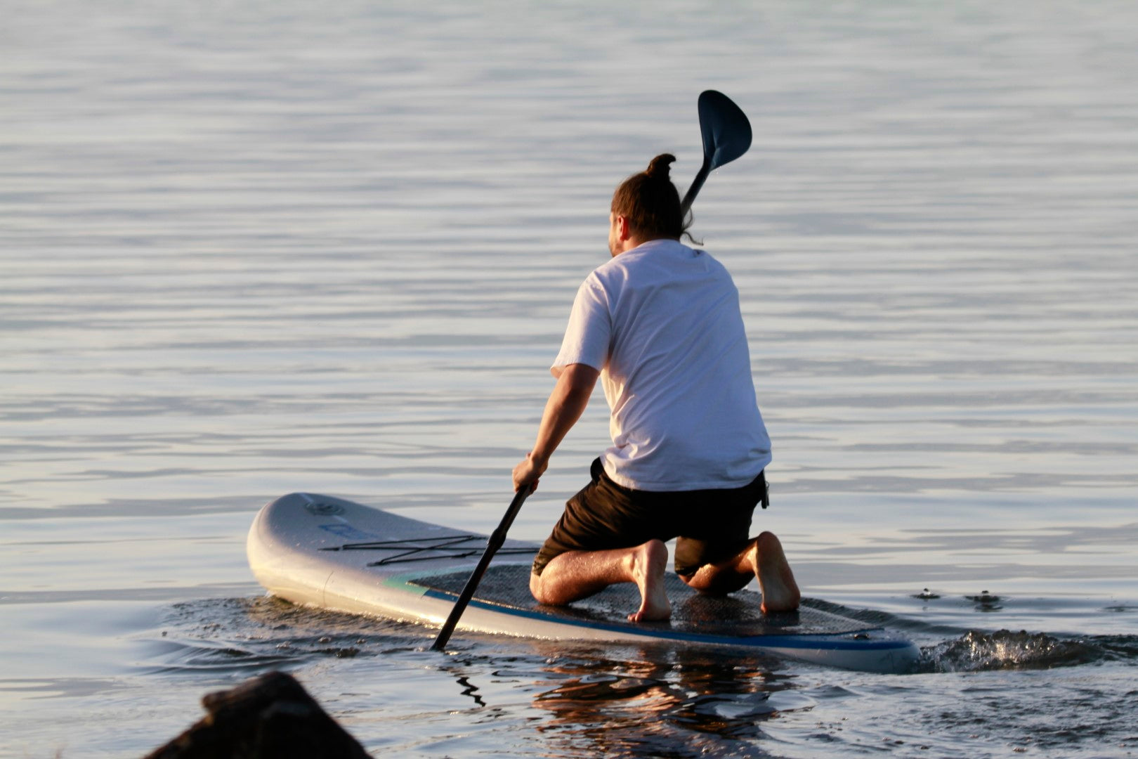 A man kneels while using the STAGE 2SIDE Double-Sided Paddleboard Paddle. The man is also using a STAGE Inflatable SUP Board.