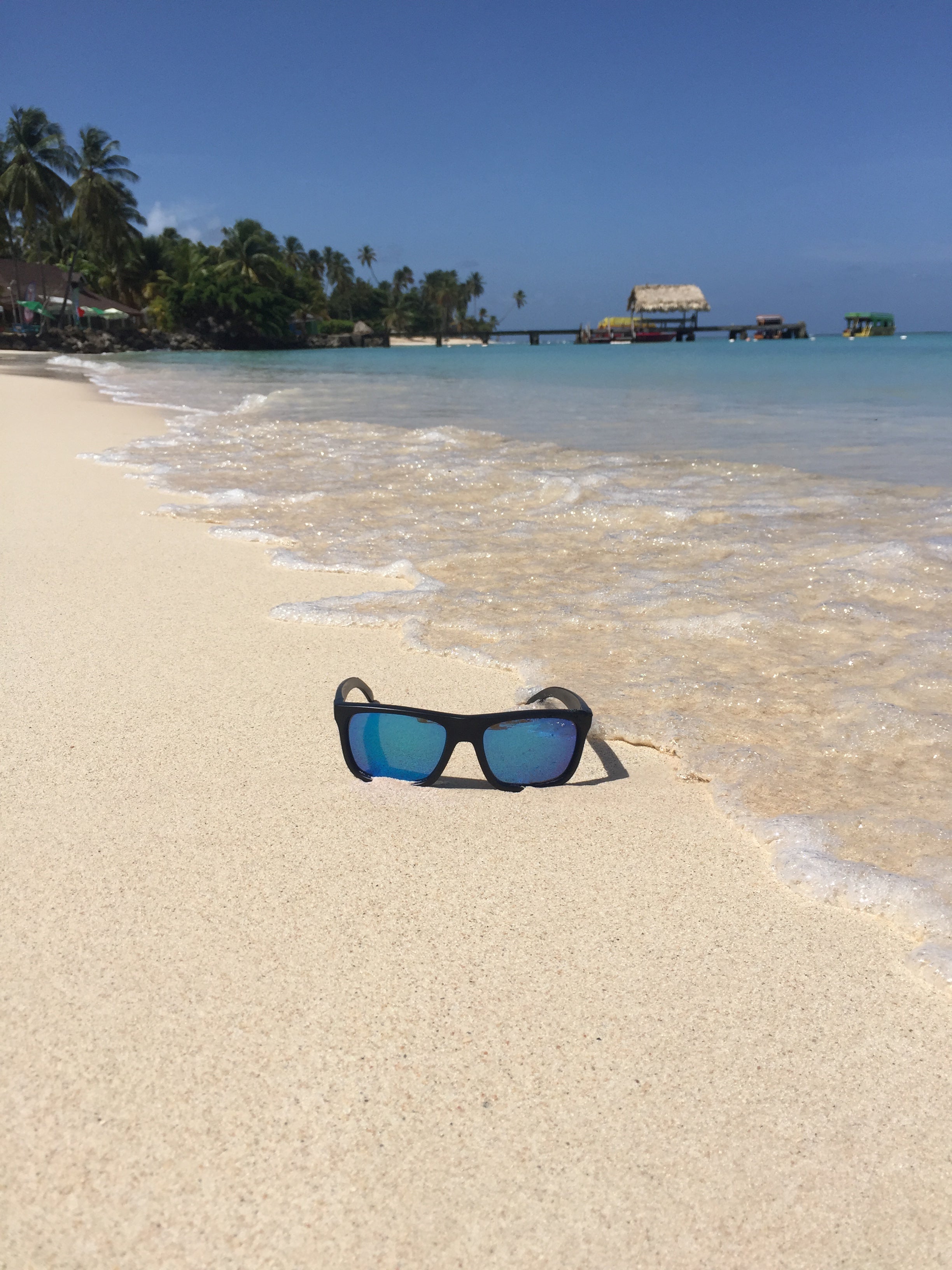 STAGE Cast Sunglasses with Blue Revo Lenses sitting on a beach with water next to them.