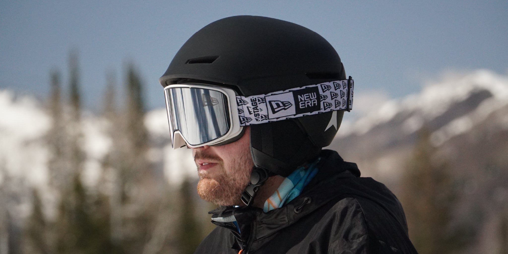 A man wearing a black Atomic ski helmet and STAGE White Prop Ski Goggle with Mirror Chrome Lens. The goggle is customized with a brand's logo to spread awareness and generate hype.