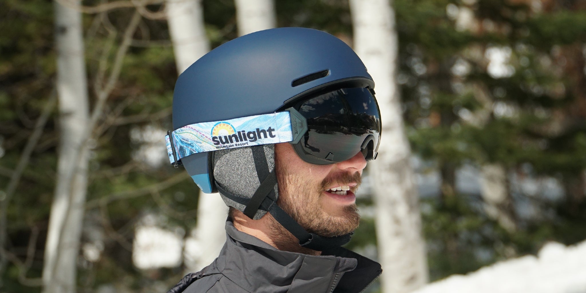 A man wearing STAGE custom ski goggles featuring Sunlight Mountain Resort's logo.