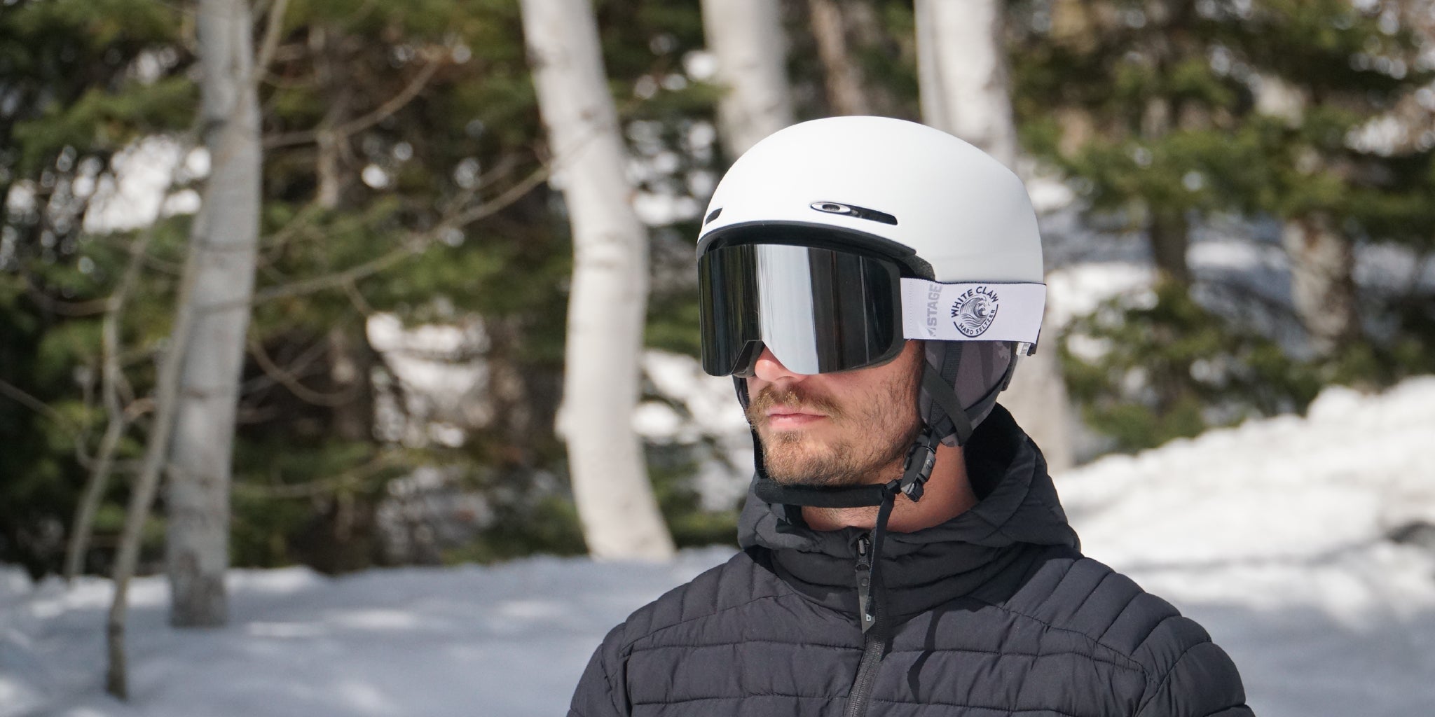 A man wearing a white oakley ski helmet and STAGE Prop Ski goggle. The goggle is customized with an organization's logo.